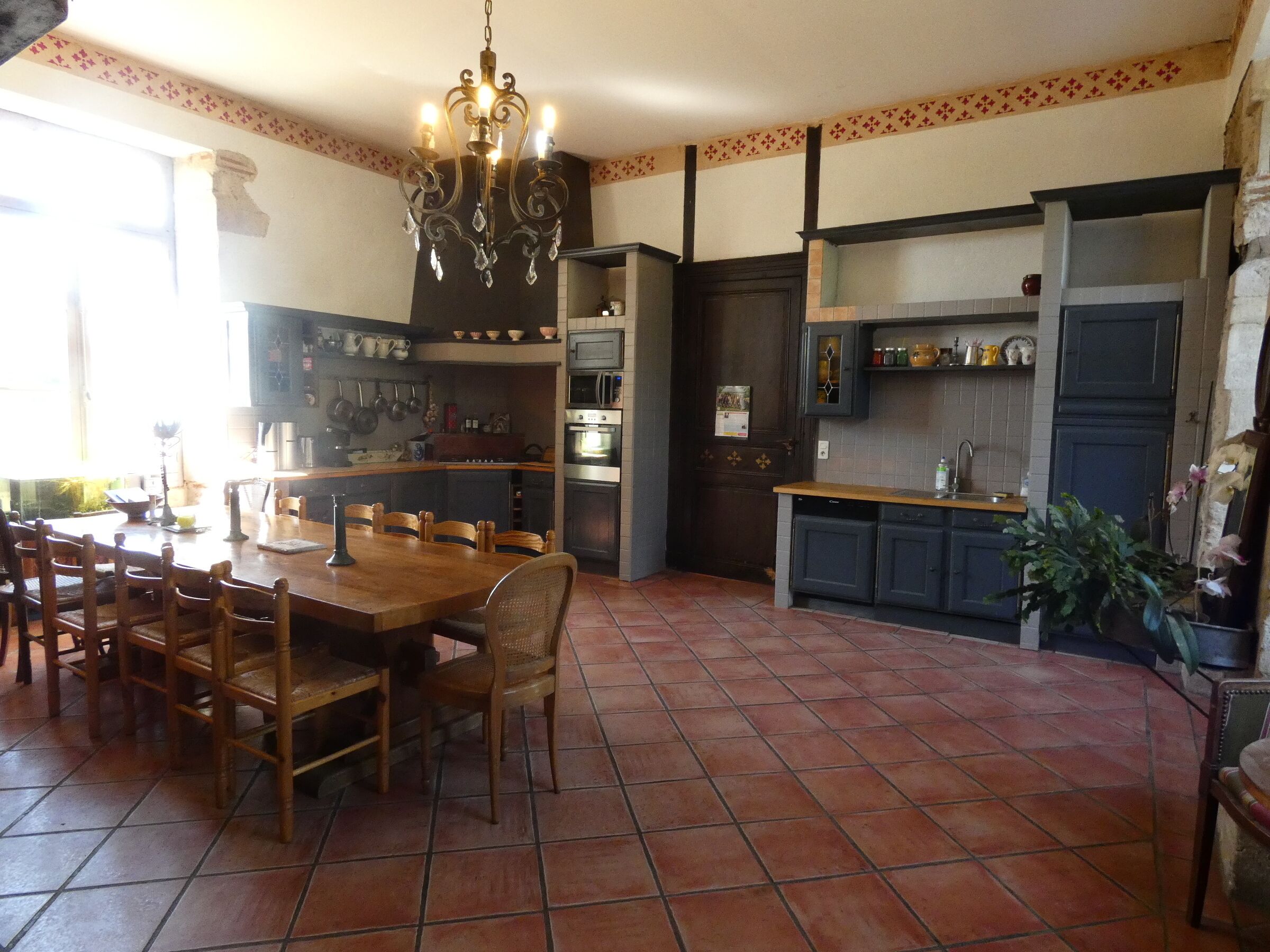 Una cocina con una mesa de comedor, sillas, una araña y suelo de baldosas.