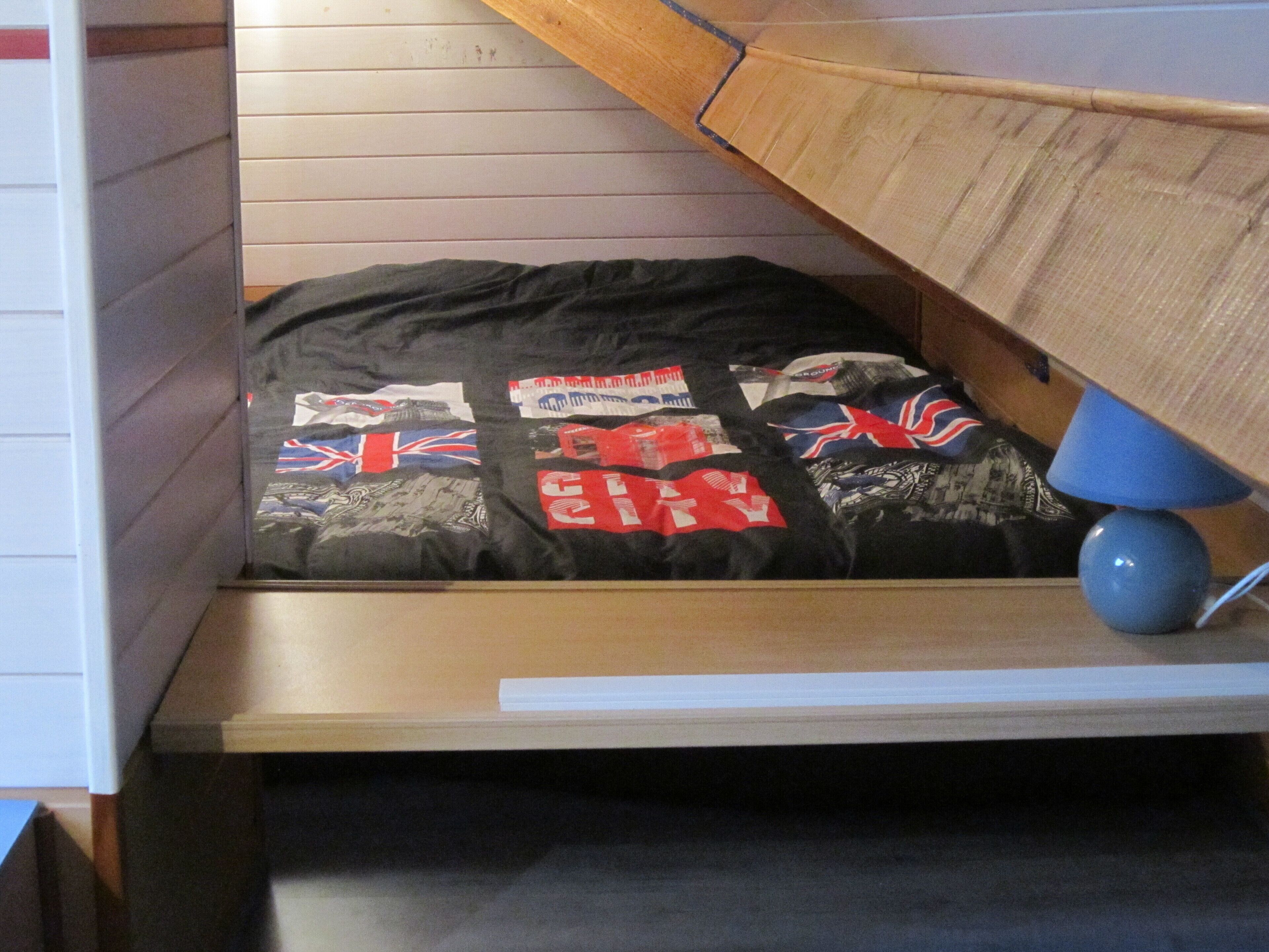 A bunk bed with a mattress featuring a Union Jack design, a blue lamp, and a wooden slanted ceiling.