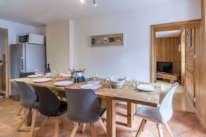 A dining area with a wooden table set for four, surrounded by chairs. A refrigerator and a television are visible in the background. - Chalet des Etoiles (11 people) Val-Cenis (Sollières-Sardières)