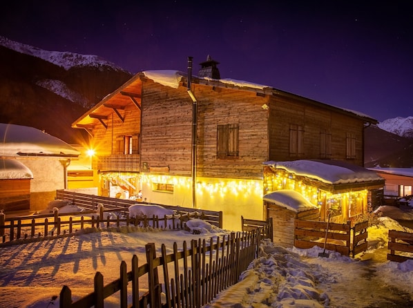 A wooden chalet with a snow-covered roof, a wooden fence, and a lit entrance. - Chalet des Etoiles (11 people) Val-Cenis (Sollières-Sardières)