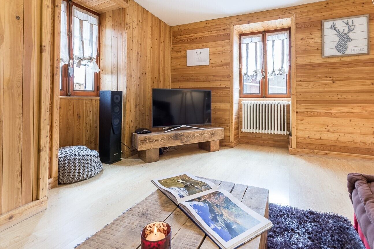 A cozy wooden cabin interior with a television, a fireplace, and a framed deer head artwork.