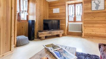 A cozy wooden cabin interior with a television, a fireplace, and a framed deer head artwork.