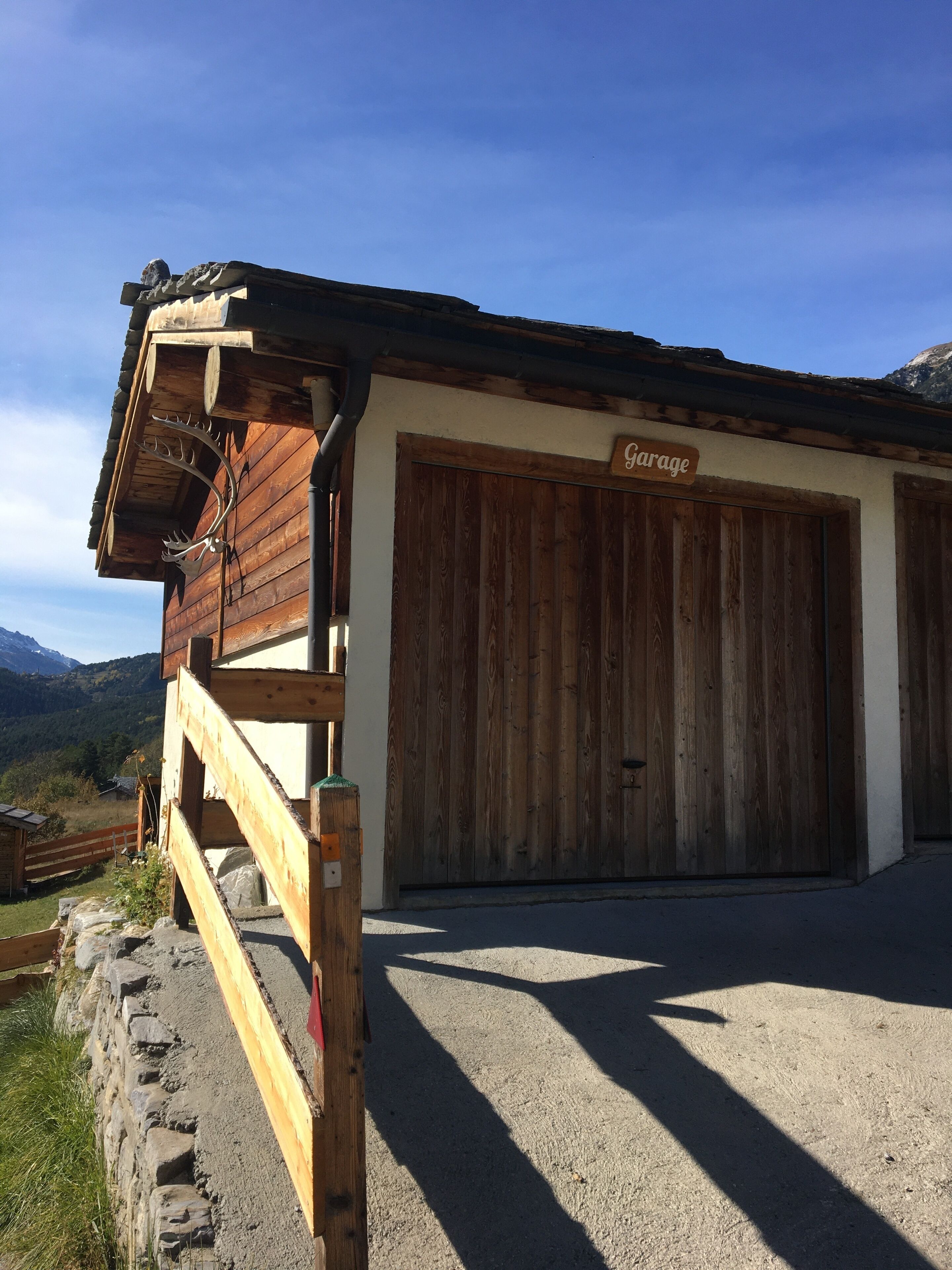 A wooden building with a garage sign, a stone wall, and a view of mountains.