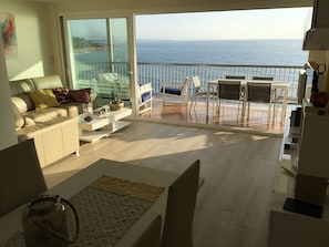 A living room with a sofa, coffee table, and a view of the sea through a glass door.