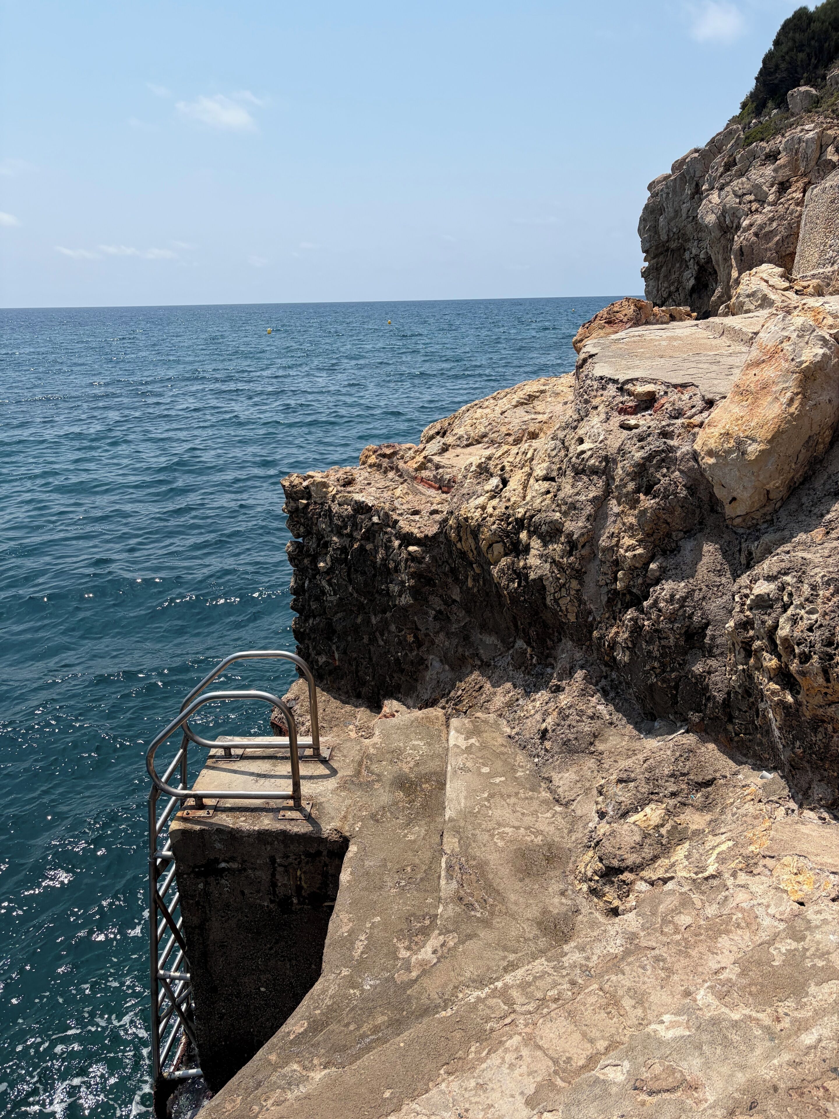 Une falaise rocheuse avec un escalier métallique qui descend jusqu'à la mer.