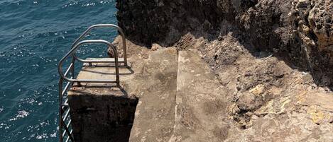 Une falaise rocheuse avec un escalier métallique qui descend jusqu'à la mer.