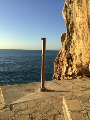 Una zona empedrada con un poste de metal, con vistas a una costa rocosa y al mar.