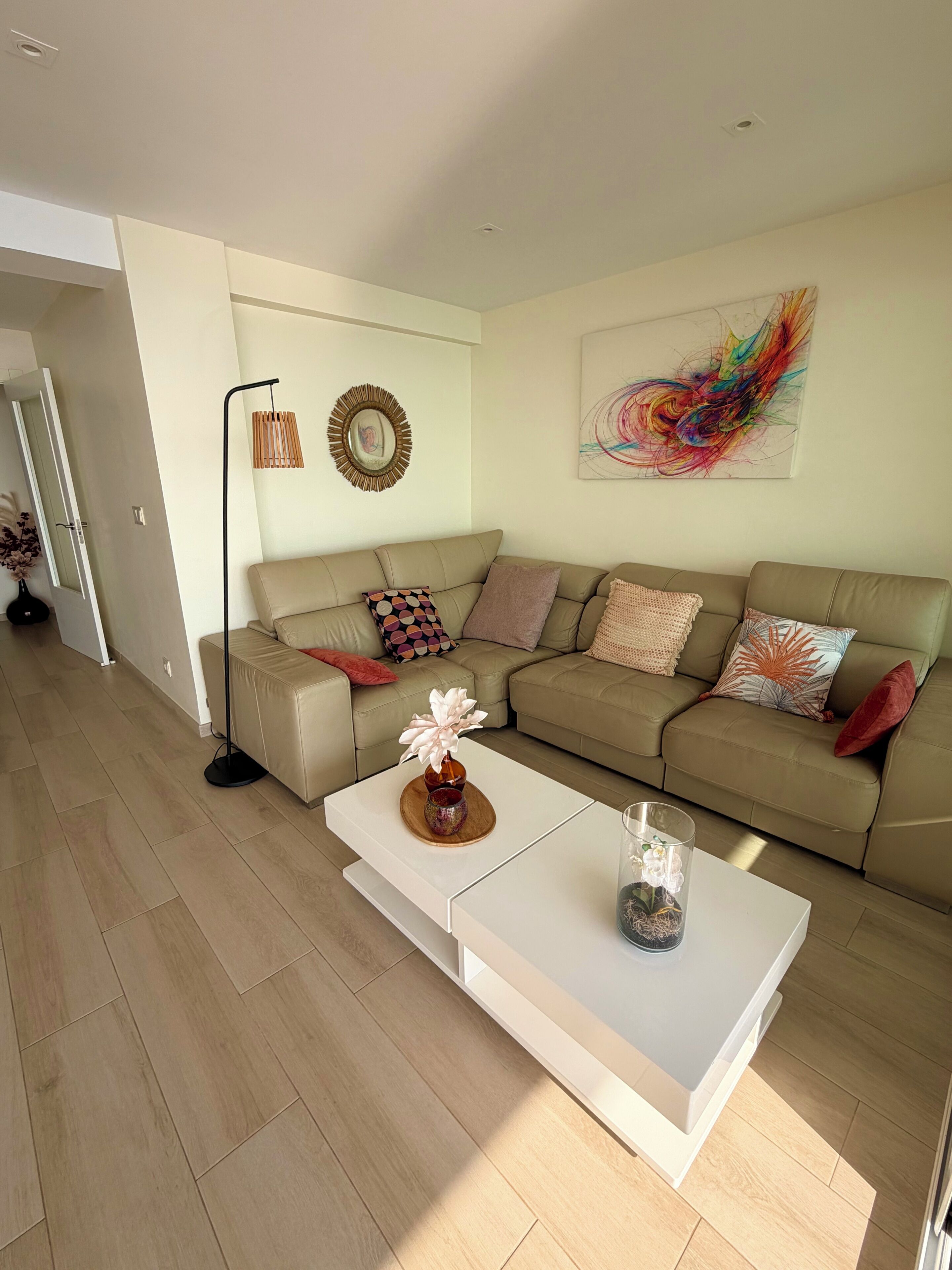 Un salon moderne avec un canapé beige, une table basse blanche et un tableau abstrait aux couleurs vives accroché au mur.