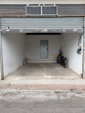 A garage with a closed metal door, a bicycle, and a yellow hose. - Salou: Beautiful air-conditioned apartment with a 180° ocean view, direct beach access, Wi-Fi, and a garage (Salou)