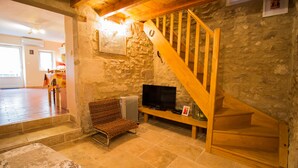 Una habitación acogedora con pared de piedra, una escalera de madera, un televisor y un banco.