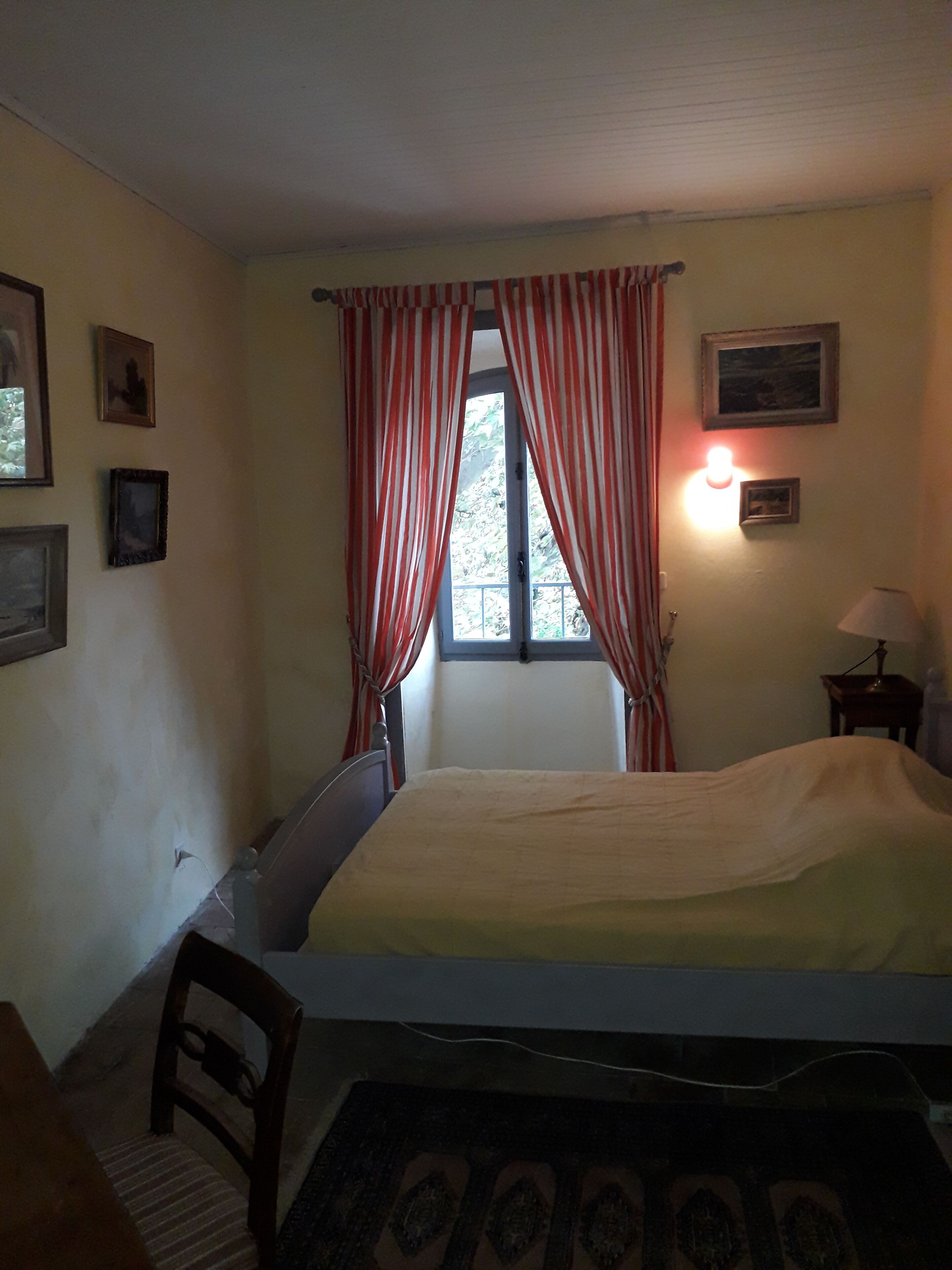 A bedroom with a bed, a chair, a window with curtains, and wall-mounted pictures.