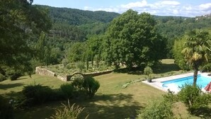 A lush landscape with a stone bridge, a swimming pool, and a view of a forested hill. - Character house in Ardèche with swimming pool, sauna and cinema (Vernon)
