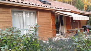 A wooden cabin with a tiled roof, a sliding glass door, and a covered patio area. - quiet house in the heart of the pine forest in pedestrian area. Near beaches (Lacanau)
