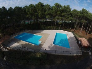 A rectangular swimming pool with a tiled deck, surrounded by a fence and trees. - quiet house in the heart of the pine forest in pedestrian area. Near beaches (Lacanau)