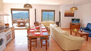 A spacious living area with a dining table set for four, a sofa, a television, and a kitchen with a washing machine. - Villa Poyatos, 15 people, Heated Pool, Wifi, BBQ, Petfriendly, sea view (Comares)