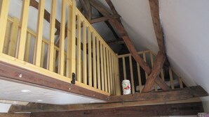 A loft-style room with exposed wooden beams, a kitchen area with a microwave, and a white bucket on the beam. - The getaway (lodging in the country) (Rodelinghem)