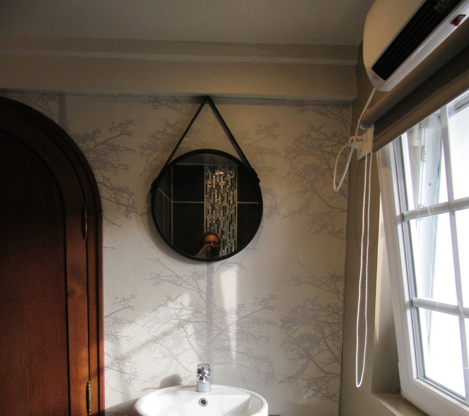 Ein Badezimmer mit einem runden Spiegel, einem Waschbecken und einem Fenster.