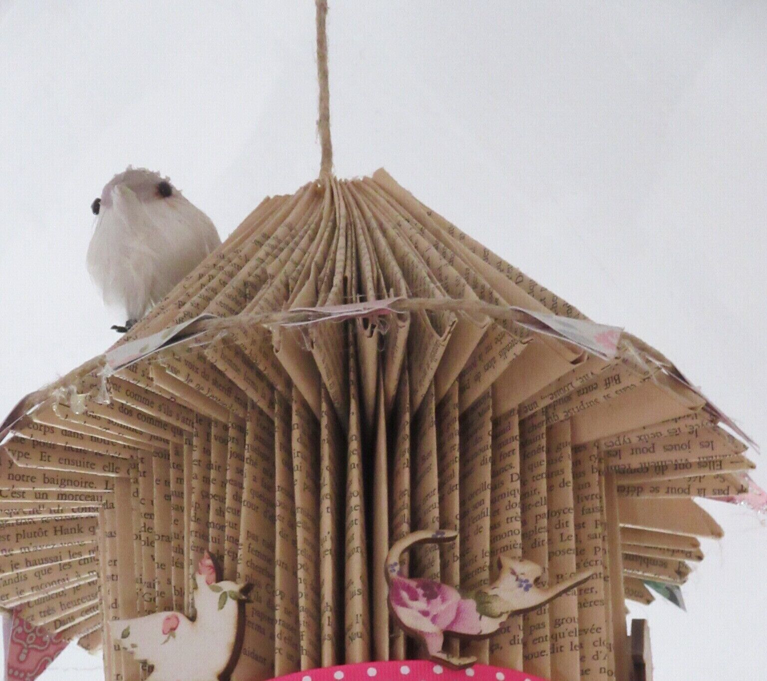 A birdhouse made of folded paper with a hanging rope, and a bird perched on it.