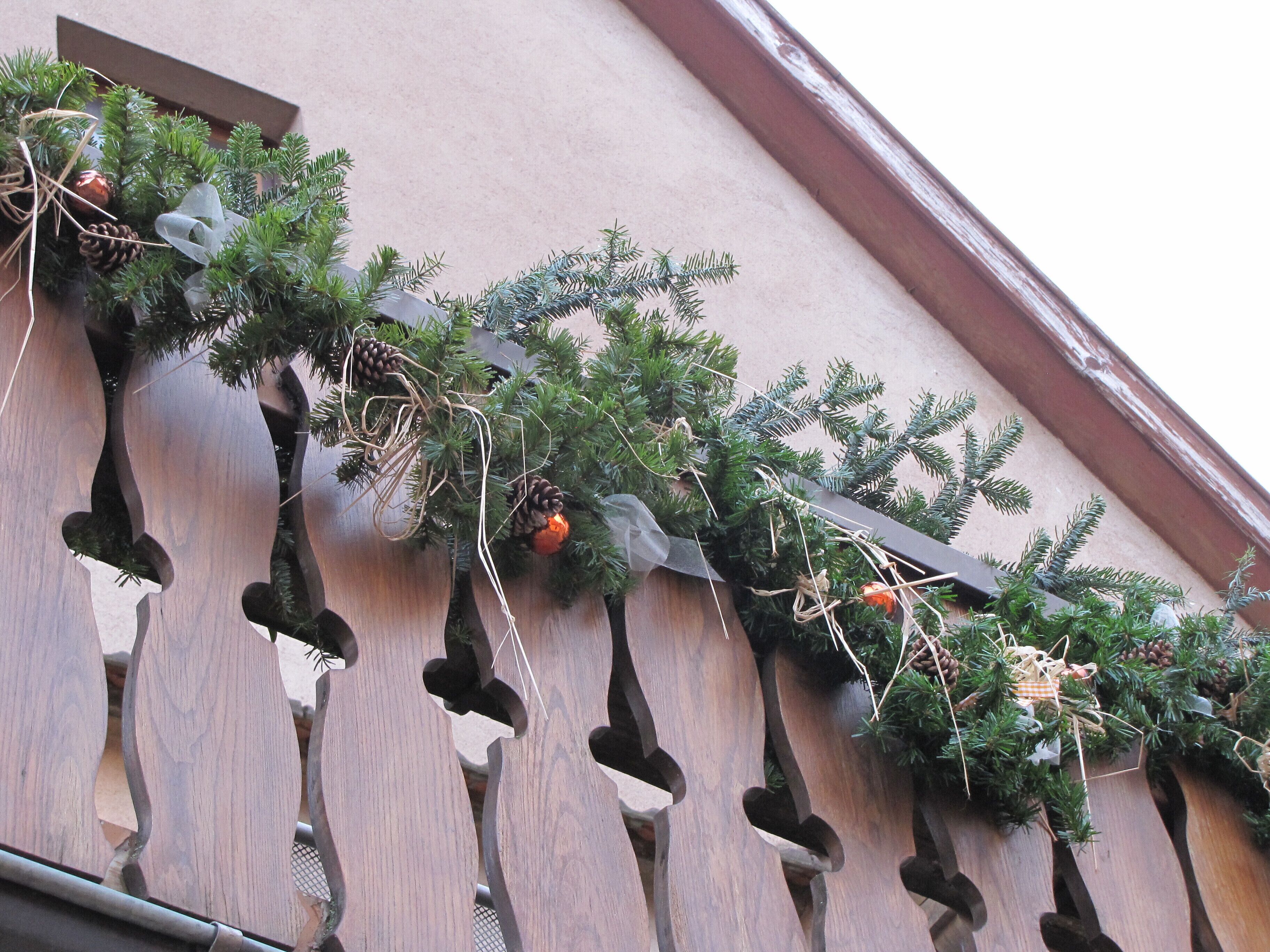 A building facade with a series of wooden planters containing evergreen branches and pine cones.