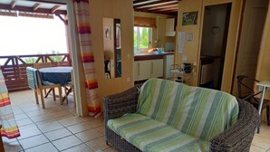 A cozy living area with a wicker sofa, a small table, and a dining table with chairs. A kitchen is visible in the background. - Chalet Filaos 2*, sea view, near Saint-Leu and its beaches  (Saint-Leu)
