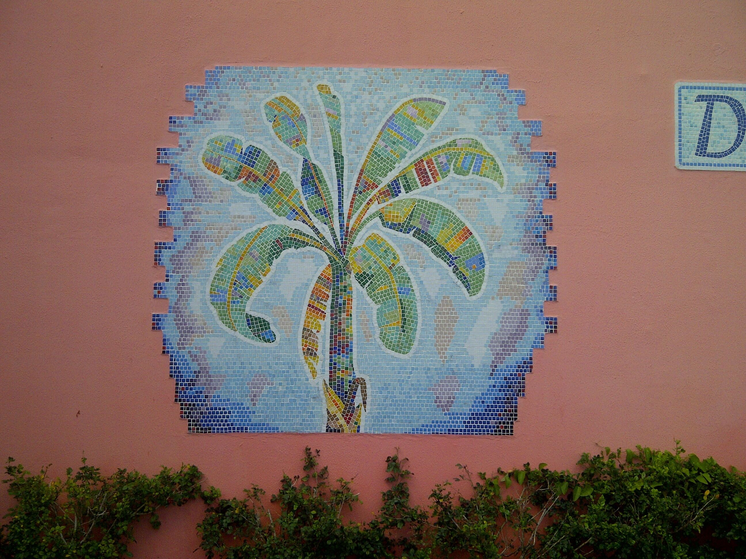 Et mosaikbillede af en palme på en lyserød væg.