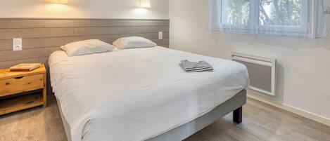 A bedroom with a bed, bedside lamps, a painting, a window with curtains, and a radiator.