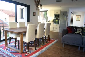 A dining area with a wooden table and chairs, a patterned rug, and a grey sofa.