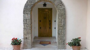 Une entrée surmontée d’une arche en pierre qui mène à une porte en bois. De part et d’autre de l’entrée, on trouve deux plantes en pot.