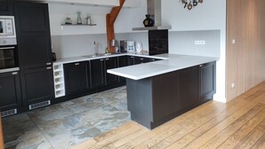 Une cuisine moderne avec des meubles de couleur sombre, un grand îlot central et un plafond en bois.