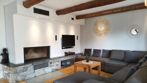 Un salon moderne avec une cheminée en pierre, un grand canapé gris, une table basse en bois et un téléviseur à écran plat fixé au mur.