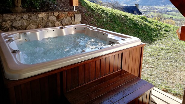Un bain à remous en bois, avec un mur en pierre en arrière-plan et une vue sur les montagnes.