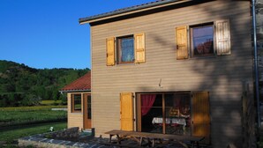 A two-story house with a stone patio, wooden shutters, and a large sliding glass door.