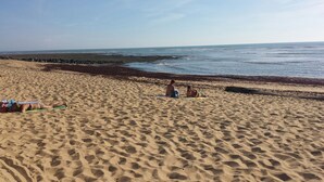 Ein Sandstrand mit zwei sitzenden und einer liegenden Person.