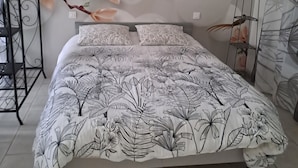 Ein Bett mit floraler Bettdecke, eine Wand mit Wandmalerei mit Blumenmuster und ein Vogelkäfig auf einem Ständer.