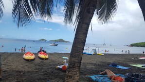 A beach with people swimming and boats in the water, a palm tree, and inflatable rafts on the sand. - CHEZ LUKETO VIEUX -HABITANTS  (Vieux Habitants)