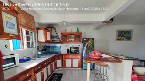 A modern kitchen with wooden cabinets, a built-in microwave, and a large island with stools. - CHEZ LUKETO VIEUX -HABITANTS  (Vieux Habitants)