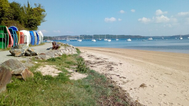 Ein Strand mit Booten im Wasser und einer Reihe bunter Kajaks am Ufer.