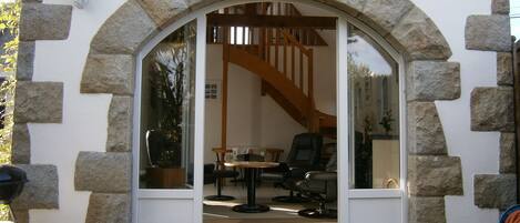 A stone-framed doorway leading into a room with a wooden staircase, a table, and a chair.