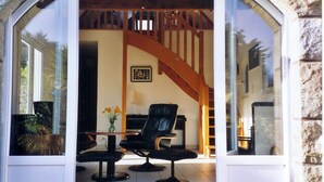 Una habitación con una escalera de madera, un sillón de cuero negro, una mesita y un florero con flores.