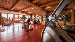 A gym with various exercise equipment, wooden ceiling beams, and large windows. - South-facing apt at the foot of the ski run. View of Tarentaise valley (Montvalezan)