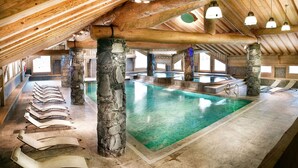 An indoor swimming pool with stone pillars, wooden beams, and multiple lounge chairs. - South-facing apt at the foot of the ski run. View of Tarentaise valley (Montvalezan)