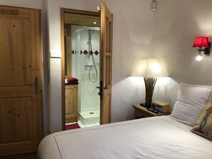 Ein Schlafzimmer mit Bett, Nachttisch mit Lampe, Holztür und Duschbereich.