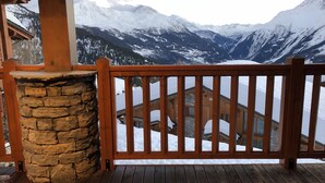 A wooden deck with a stone pillar, wooden railing, and a view of snow-covered mountains. - South-facing apt at the foot of the ski run. View of Tarentaise valley (Montvalezan)