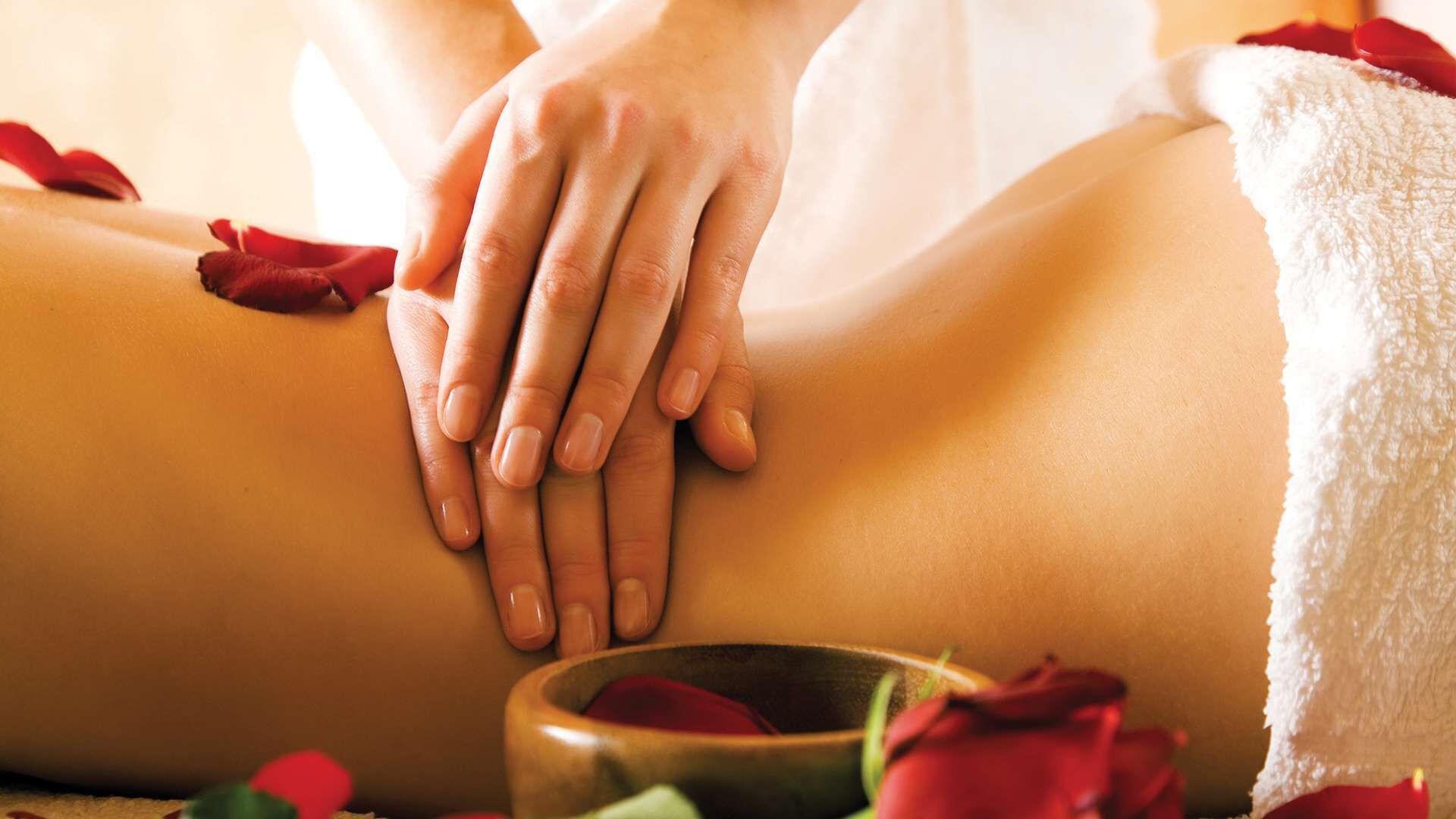 A close-up of hands performing a massage on a person's back, surrounded by rose petals.