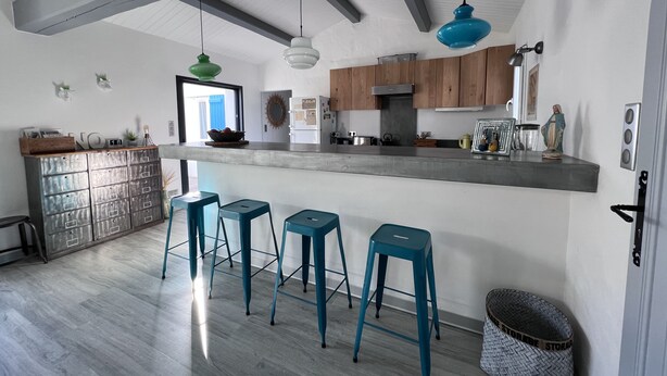 A modern kitchen with a bar area, wooden cabinets, and blue bar stools. - Holiday house in Noirmoutier at 150m from the beach (Noirmoutier-En-L'île)