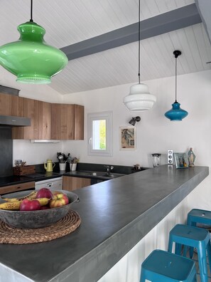 A modern kitchen with a large island, wooden cabinets, and pendant lighting.