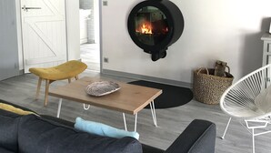Un salon moderne avec une cheminée en pierre, un canapé, une table basse en bois et un fauteuil blanc.