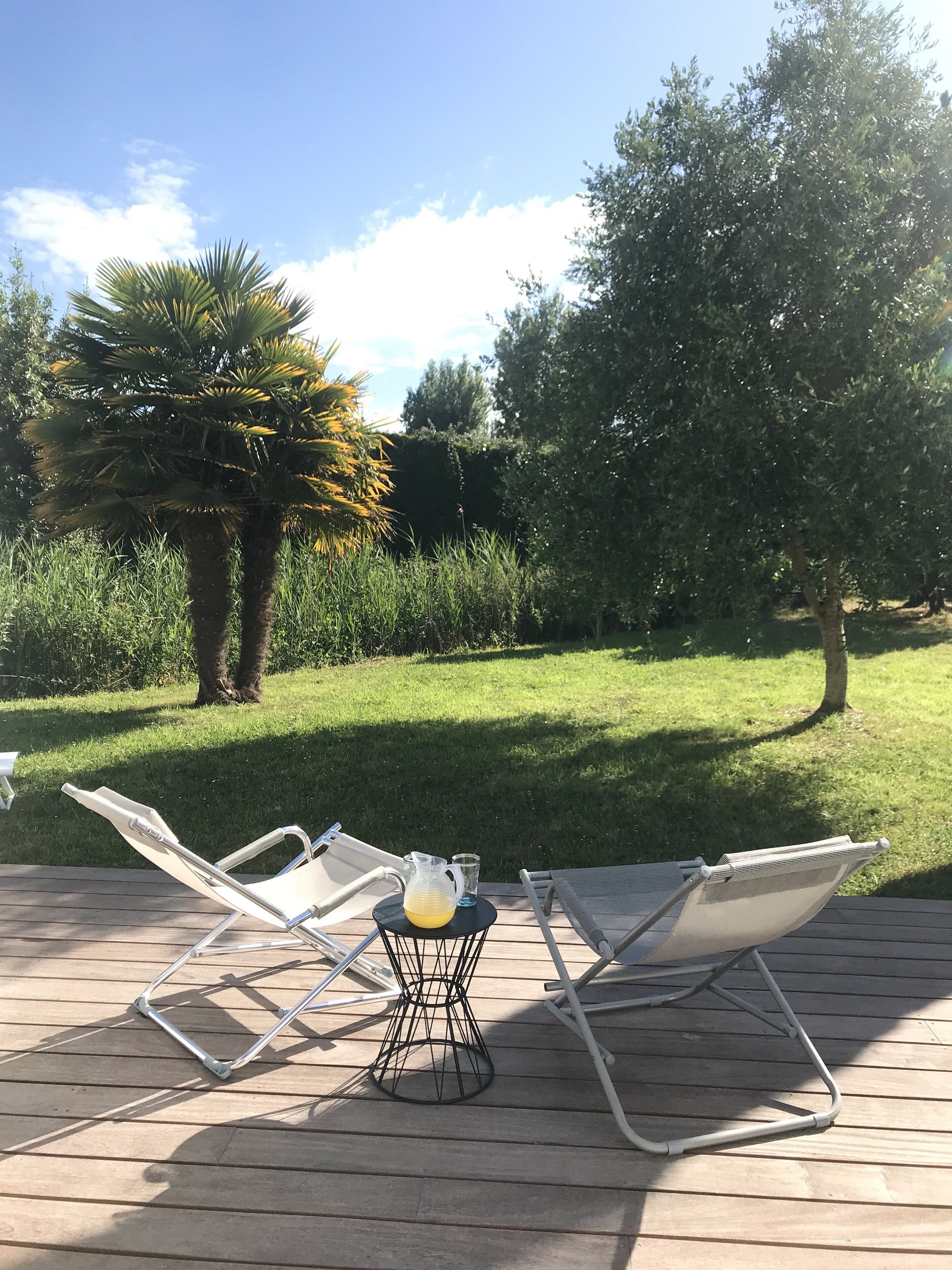 Une terrasse avec deux chaises longues et une petite table sur laquelle se trouvent une carafe et un verre.