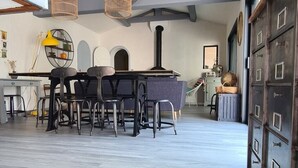 Une pièce spacieuse avec un plafond haut, des poutres apparentes, un coin repas avec une table et des chaises, et une grande armoire à plusieurs portes.