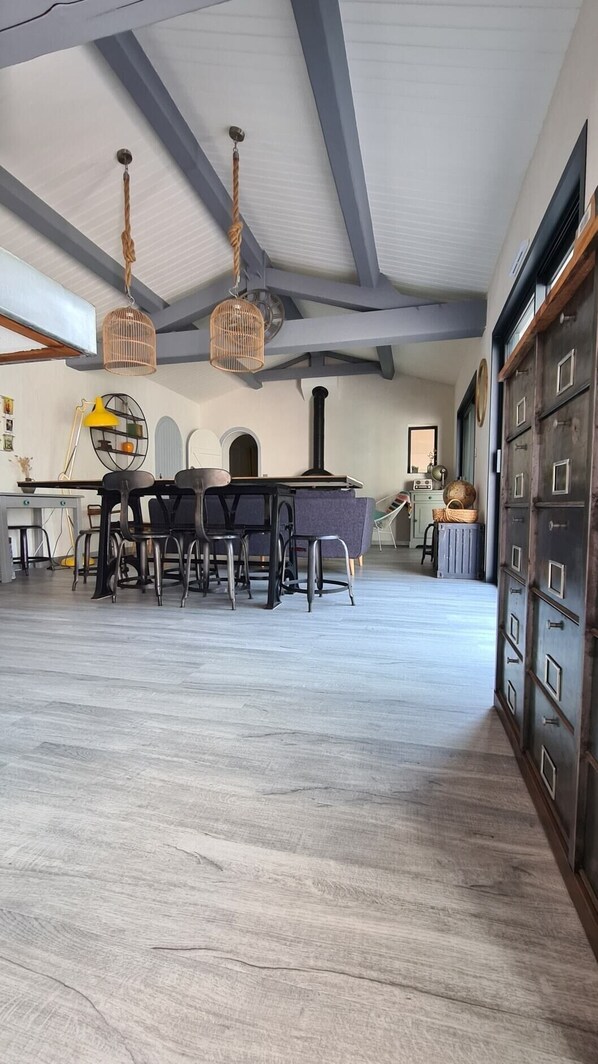 Una habitación amplia con techo alto, vigas a la vista, un comedor con mesa y sillas, y un vestidor grande con múltiples puertas.